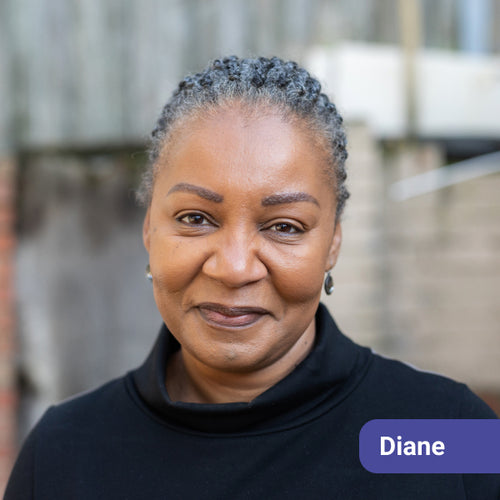 Woman with gray hair wearing a black turtleneck, with a name tag labeled 'Diane' standing outdoors with a blurred background.
