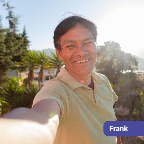 Man taking a selfie outdoors with palm trees and clear sky in the background, with a name tag labeled 'Frank'.
