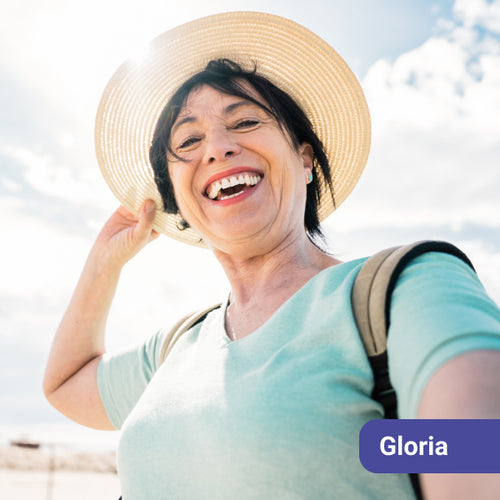 Woman wearing a straw hat and light blue shirt with a backpack, outdoors with a name tag labeled 'Gloria'.