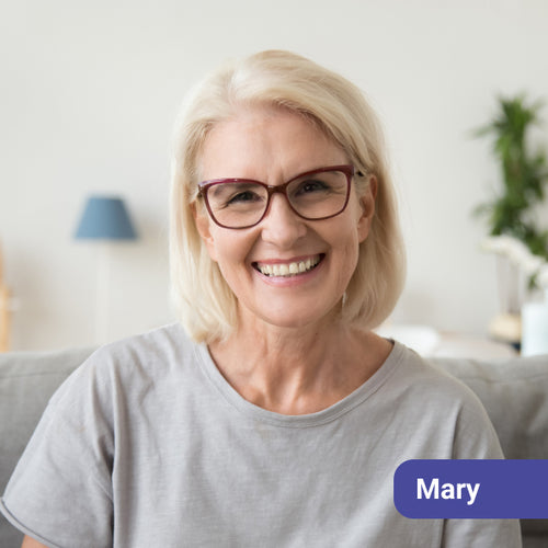 Woman with glasses smiling in a living room setting, with a name tag labeled 'Mary'.