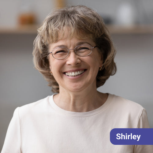 Woman with glasses smiling, with a name tag labeled 'Shirley' on a blurred background