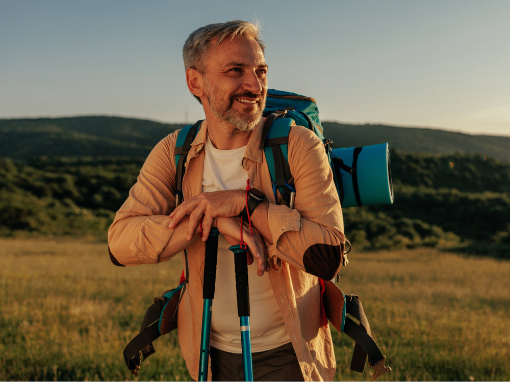 Man with hiking backpack and poles standing in a field with mountains in the background