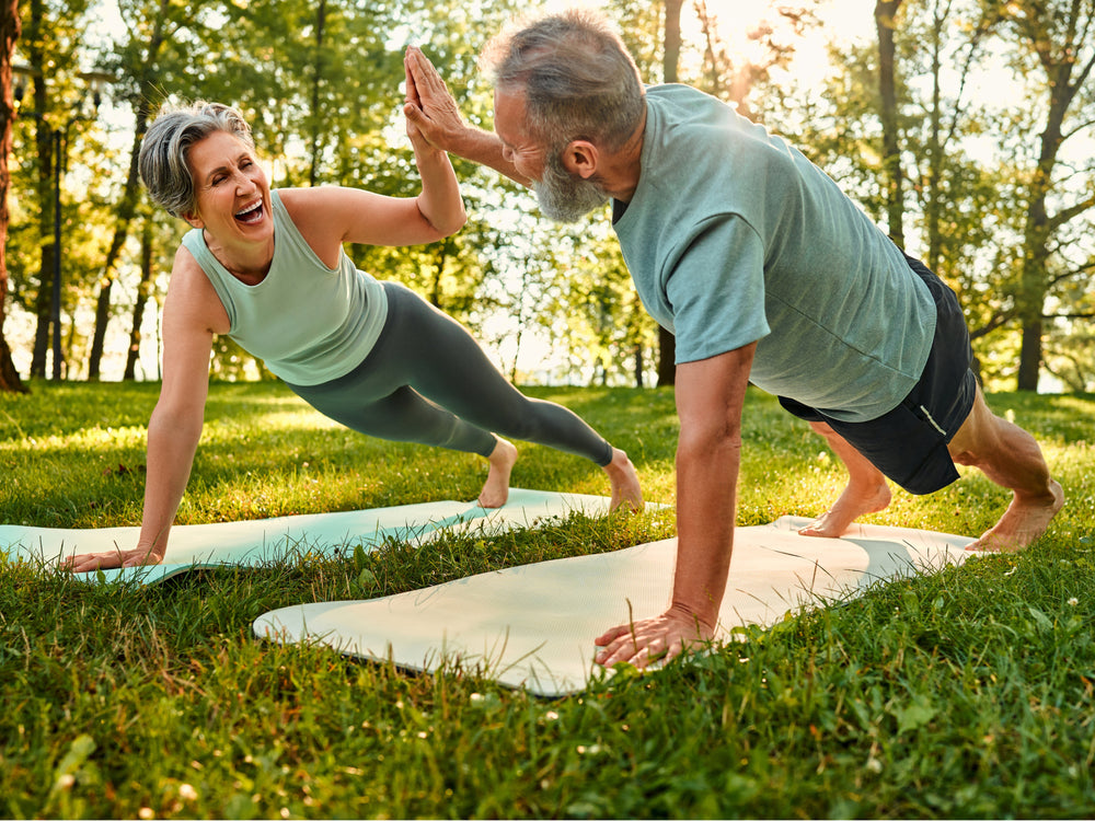 Two people doing yoga on grass with trees in the background